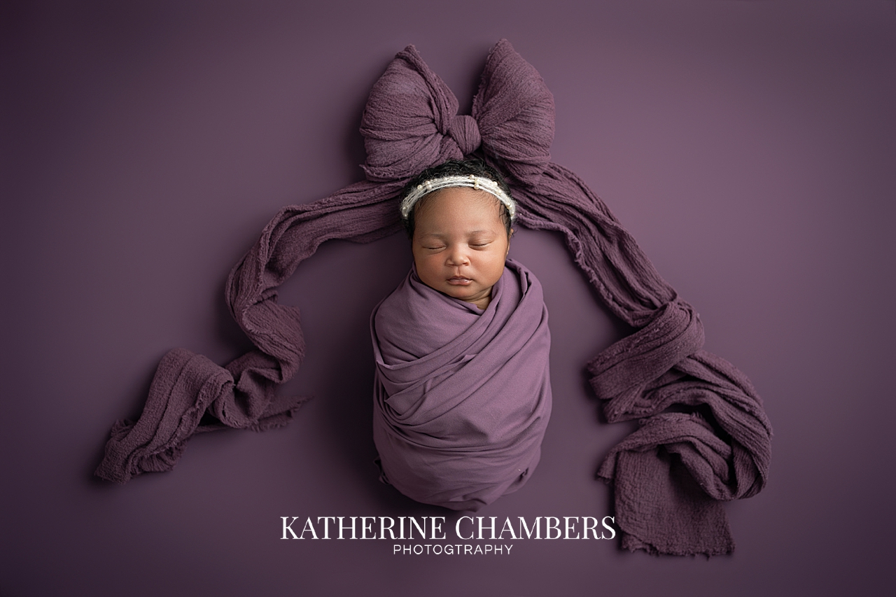 Newborn baby girl in deep purple/plum wrap and bow