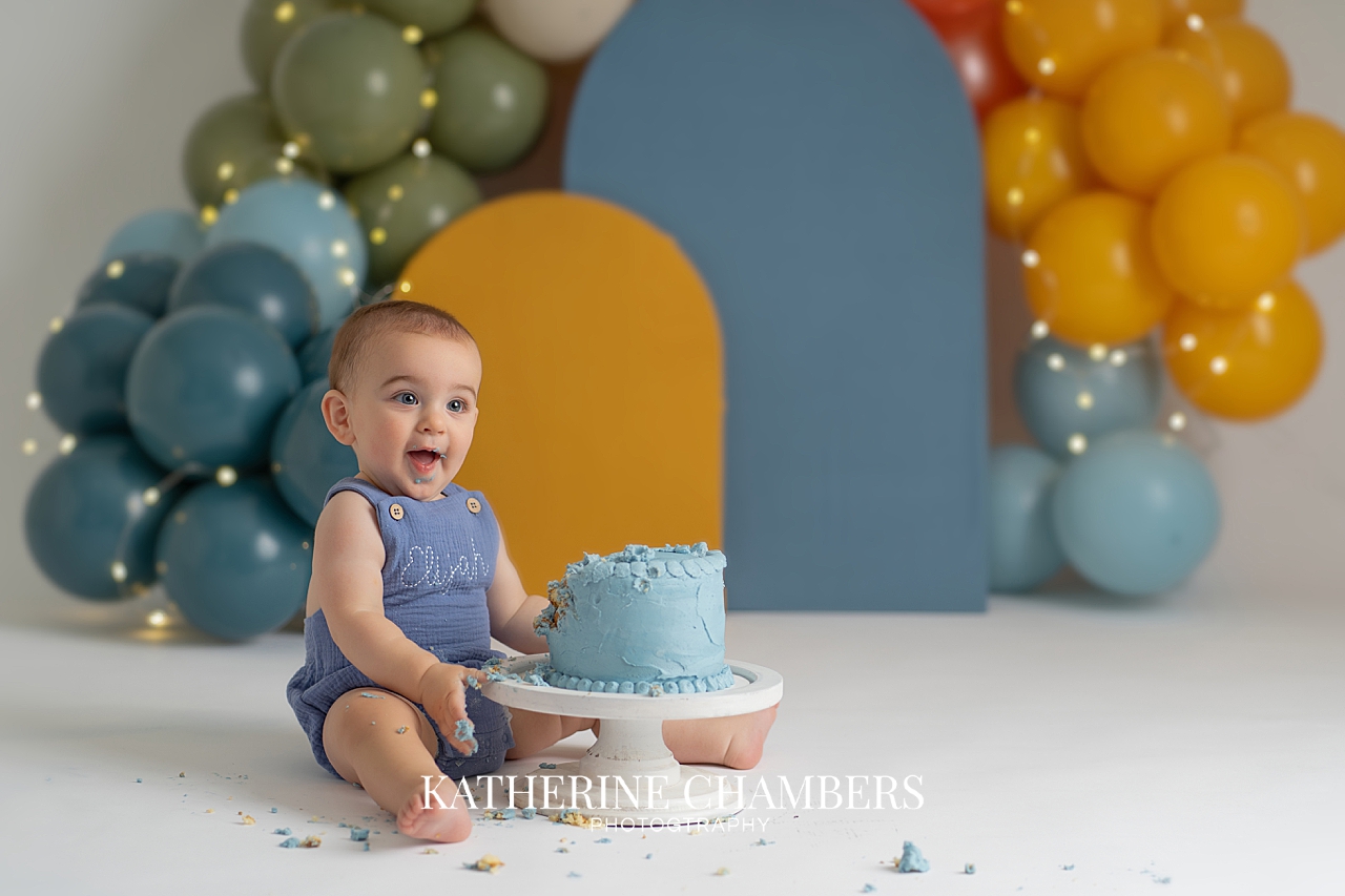 Happy baby Elijah smiling during his colorful first birthday cake smash photography session